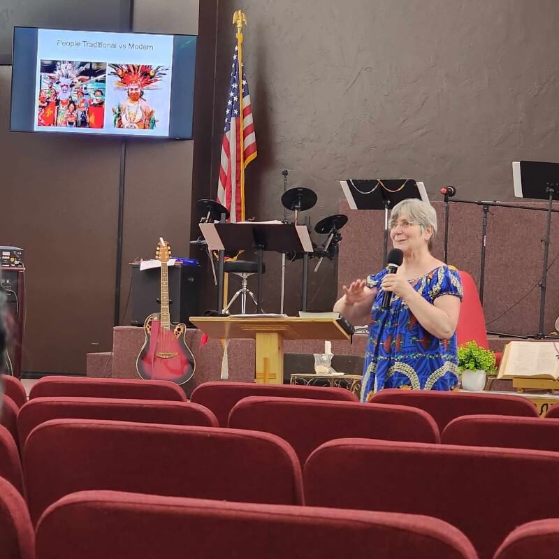 A woman at the microphone in church in front of red pews
