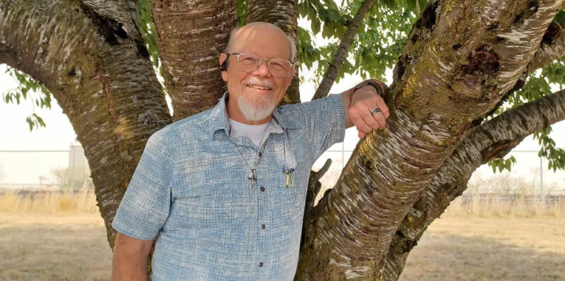 Image of Pastor Will smiling at the camera and putting his arm up against a tree